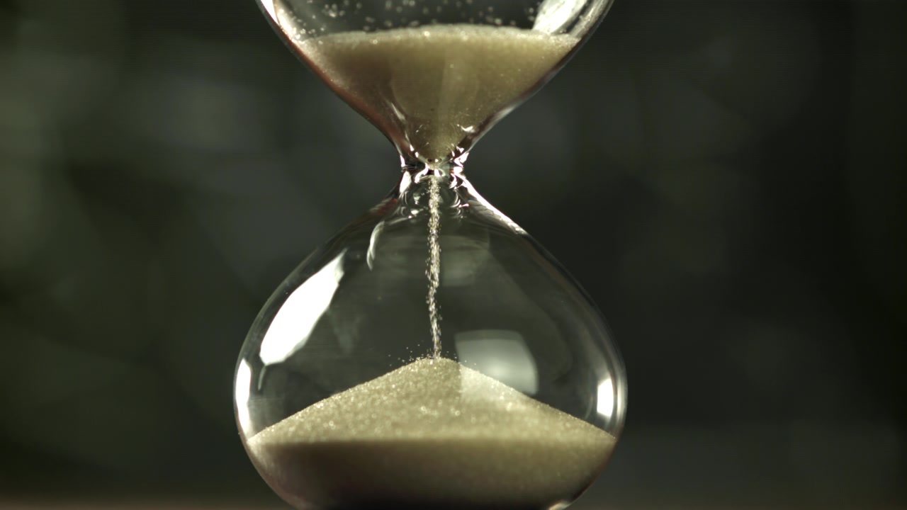 Sand Flowing Through a Glass Hourglass on Dark Background