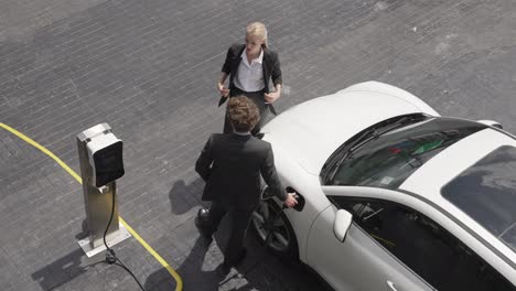 progressive businessman and businesswoman leaning on ev car and charging point.