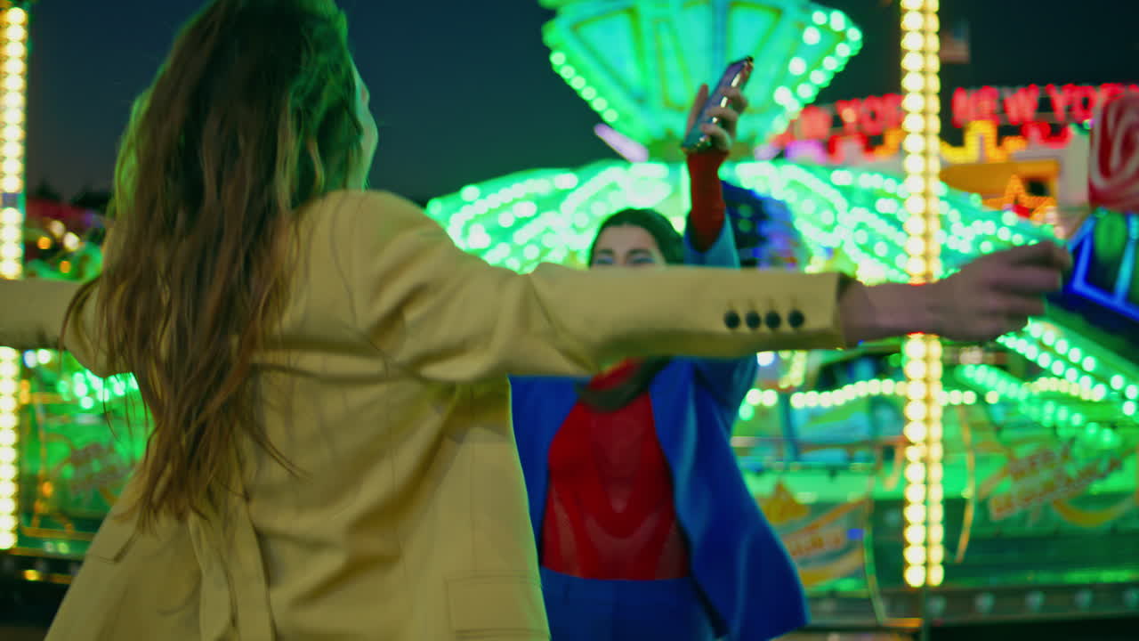 쾌활한 친구들이 밤에 놀이공원에서 만나고 행복한 미소 짓는 소녀들이 포옹합니다.