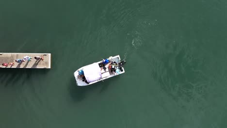 Small-motorboat-docking-at-narrow-dock-with-people-aerial-straight-down