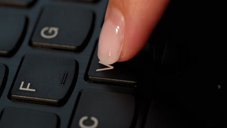 Black keyboard and a girl presses V button. English letters. Slow-mo and girl has a pink nail polish.