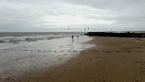 two-people-on-deserted-Beach-kit-surfers-in-background-Clacton-on-Sea-Essex-England