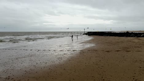 two people on deserted beach kit surfers in background clacton on sea essex england