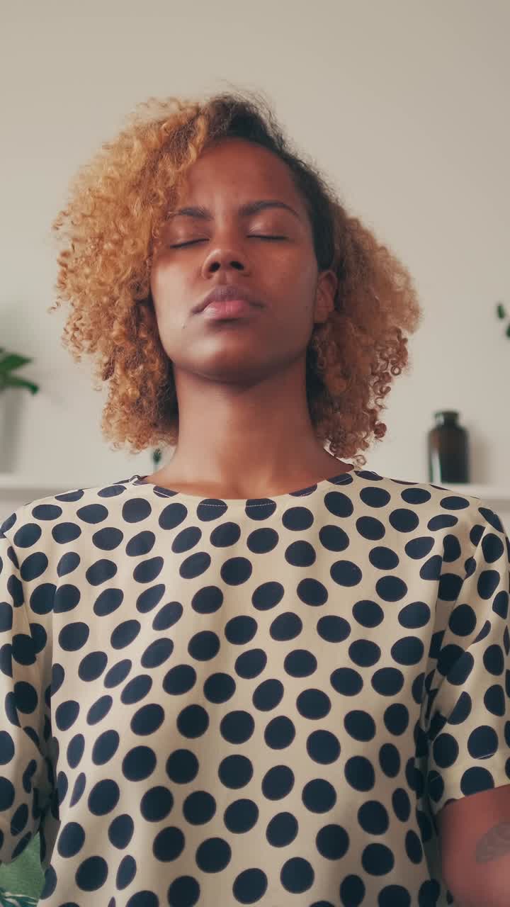 Young peaceful african american woman doing yoga sits in lotus position on sofa