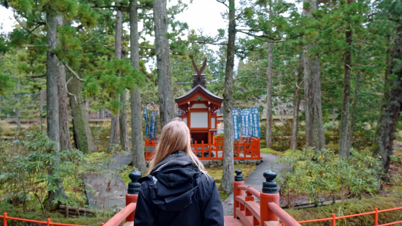A cinematic scene capturing a blonde girl walking gracefully across a traditional bridge within the sacred grounds of Danjo Garan in Mount Koya, Koyasan, Japan.
