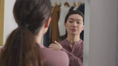 young woman at home putting on outfit for job interview reflected in mirror