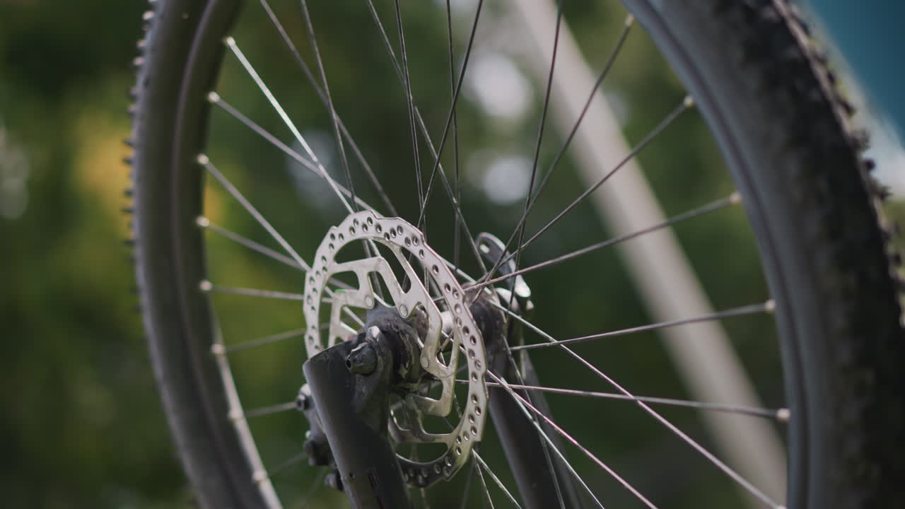 closeup bicycle disc brake with droplets on rotor, spokes and knobby tire, shallow depth of field, green blurred background, quiet maintenance atmosphere, mechanic inspection mood
