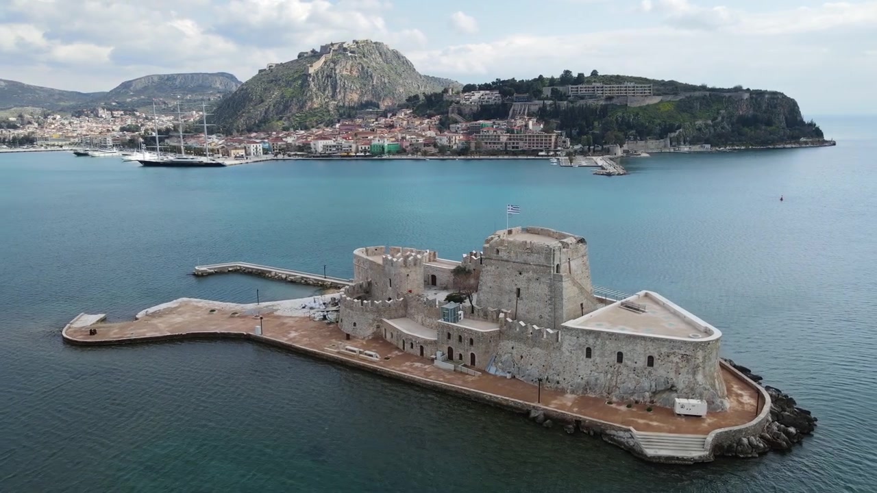 Il castello di Bourtzi sorge su una piccola isola nel porto di Nauplia, con acque blu calme che circondano la storica fortezza. La vista aerea rivela la città costiera e le montagne sullo sfondo