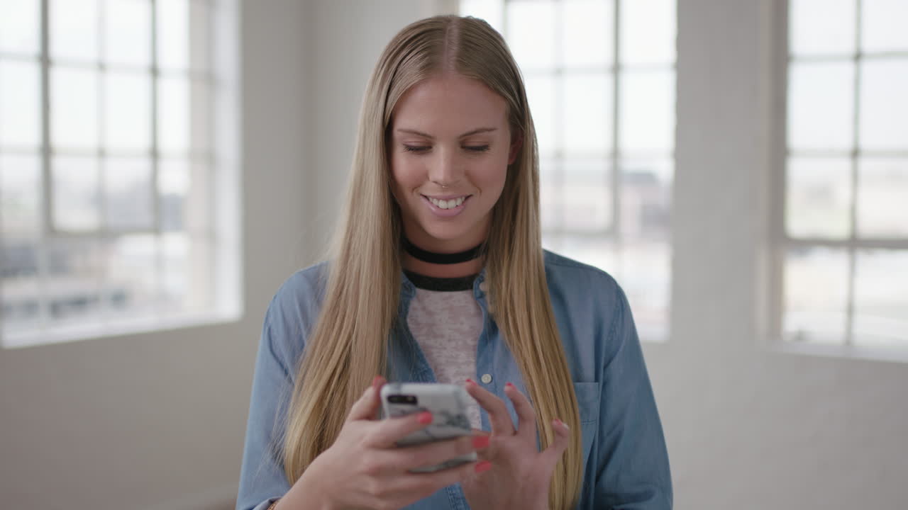 ritratto in slow motion di una bellissima giovane donna bionda in un nuovo appartamento che scrive messaggi navigando utilizzando lo smartphone tecnologia mobile felice eccitato