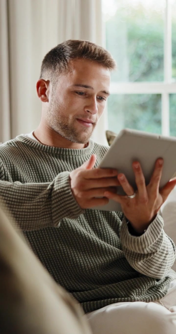 Ung far, der bruger en tablet, mens han slapper af i sofaen derhjemme