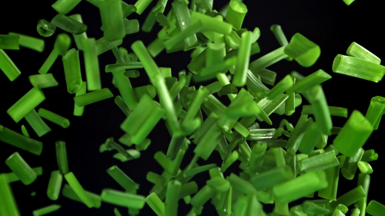 Hakkede forårsløg falder i slowmotion på sort baggrund.