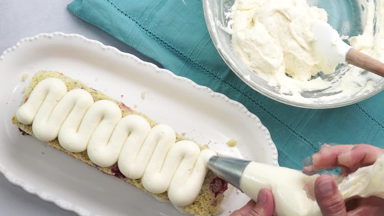 Making a dessert called Red Raspberry Tea Cake made with fresh berries and vanilla buttercream frosting. Great for Tea Parties. Piping vanilla buttercream frosting to the top of the layer cake