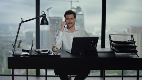 Businessman-talking-on-smartphone-at-workplace.-Man-sitting-at-table-with-laptop