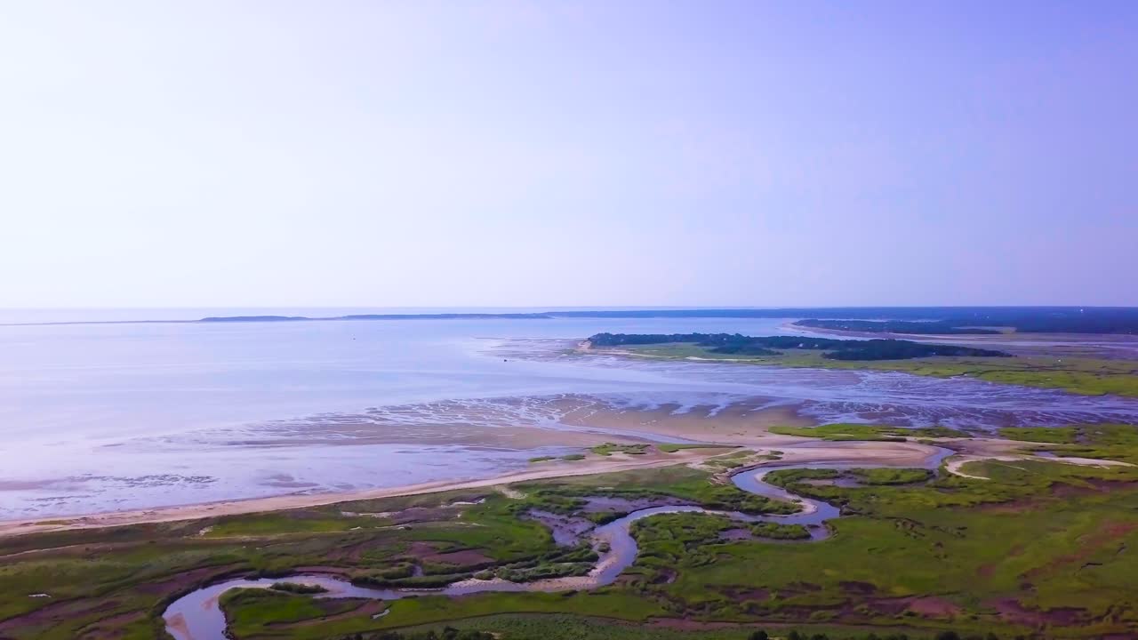 Sunken Meadows on Cape Cod, MA. The marsh and channels of water connect to the bay. The tide is low and much of the beach is freshly exposed. The camera pulls out revealing more of the marsh.