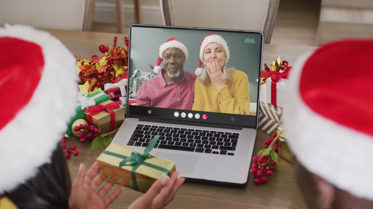 animación de una pareja diversa con sombreros de papá noel en una llamada de video portátil con amigos en navidad