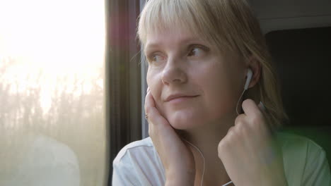 a woman listens to music on headphones looks out the window from a traveling train travel and holida