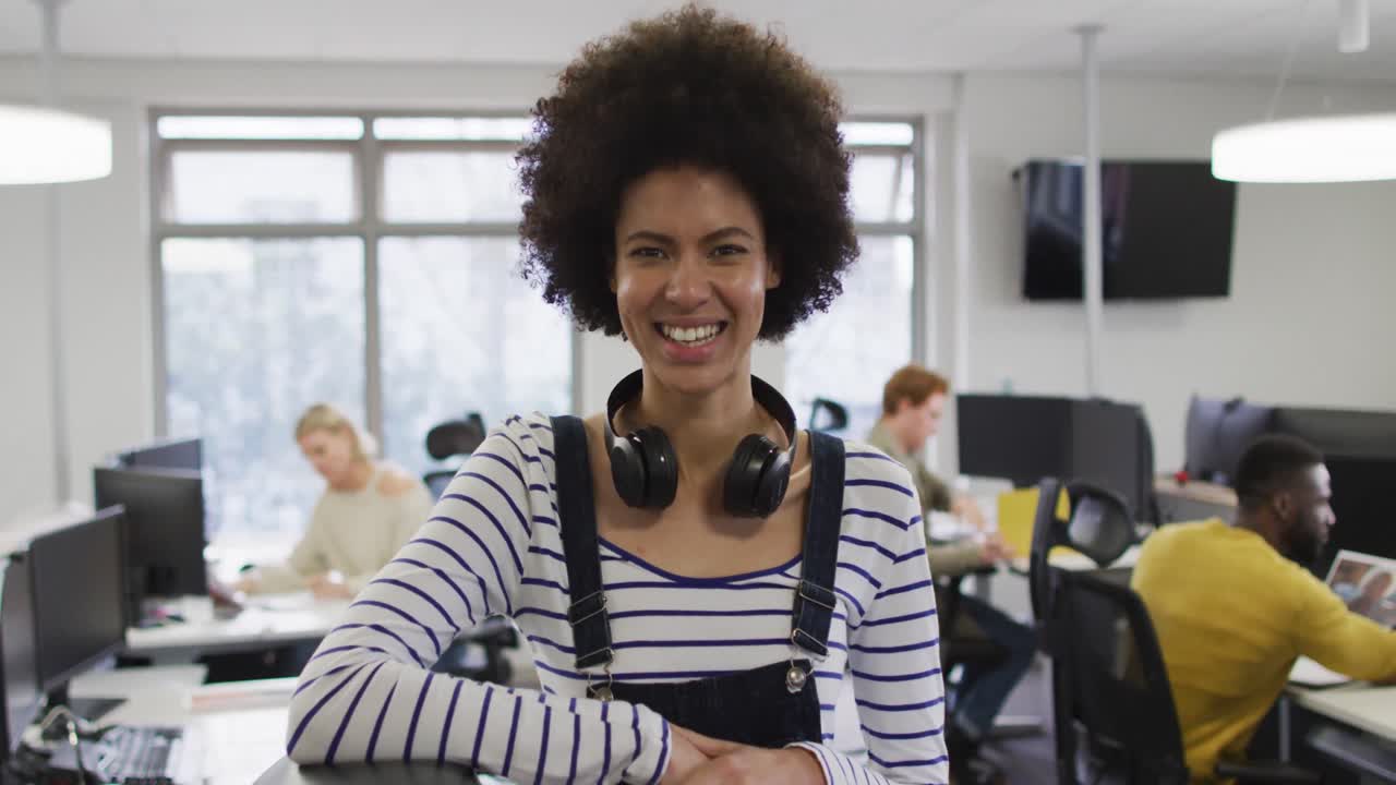 retrato de uma mulher de negócios afro-americana sorridente e criativa sentada à mesa em um escritório moderno