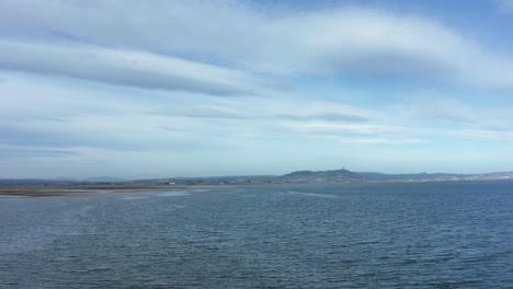 Scrabo-tower-drone-flight-over-water-on-bright-blue-sunny-day