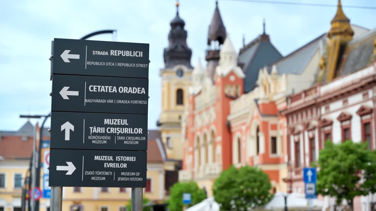 View of a sign showing directions to popular places on the Unirii Square with multiple old buildings made in classic style on the background in Oradea, Romania
