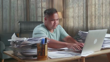 hombre gordo asiático usando una computadora portátil y luego tomando notas mientras trabaja con documentos en la oficina