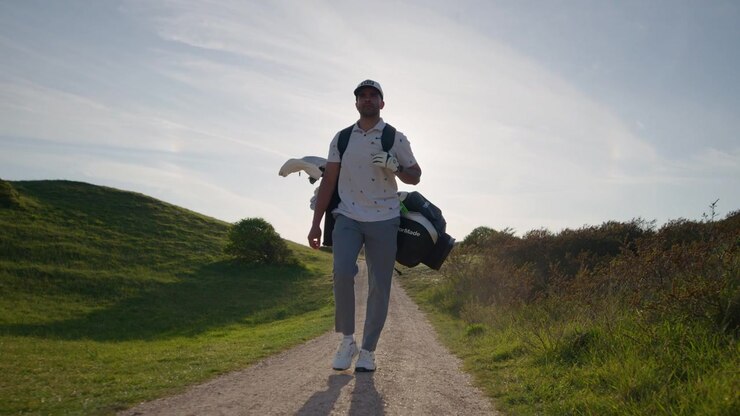 Golfista professionista uomo cammina sul campo durante l'ora d'oro, ripresa frontale al rallentatore.