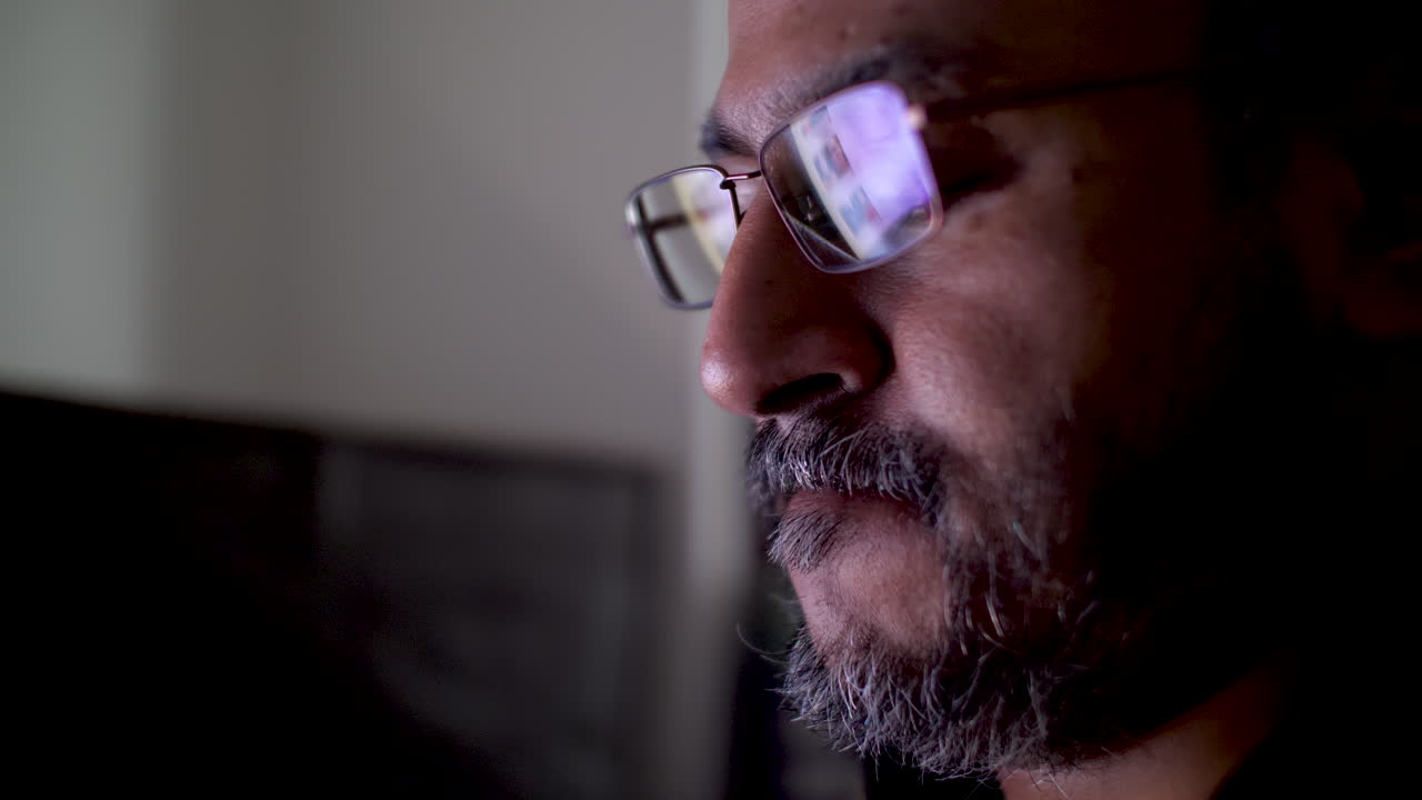 Close up of a South Asian man wearing glasses with a monitor reflection