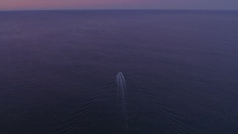 Flying-backwards-and-seee-small-motorboat-cruising-on-calm-ocean-with-sunrise-Portugal,-aerial