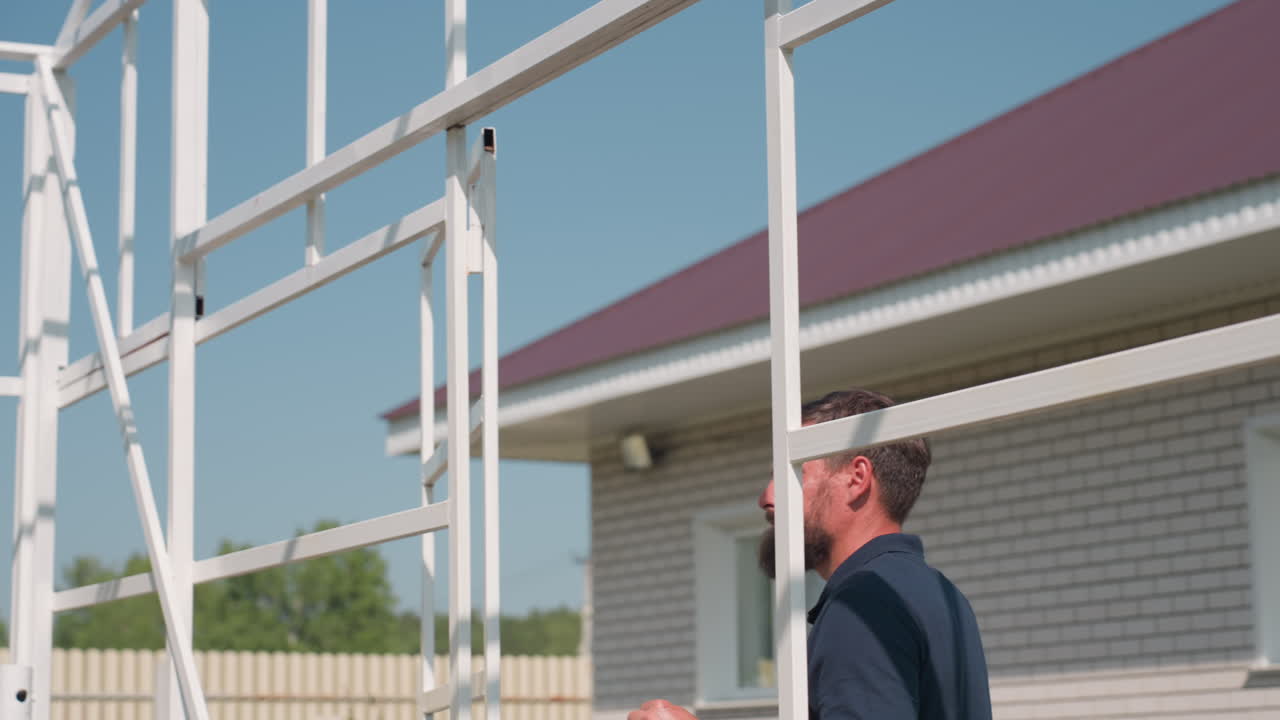 man aiming gun then lowering while watching target, tense focus in outdoor farm setting with white frame structure and trees, sunlight highlighting concentration during pest control and inspection