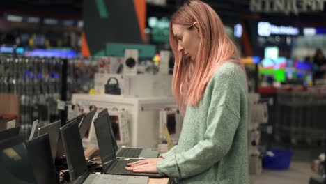 mujer elige una computadora portátil en una tienda de dispositivos, seleccionando cuidadosamente