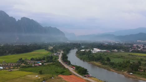 Luftaufnahme-Von-Vang-Vieng-Am-Abend-Mit-Dem-Fluss-Nam-Song,-Der-Durch-Die-Landschaft-Fließt