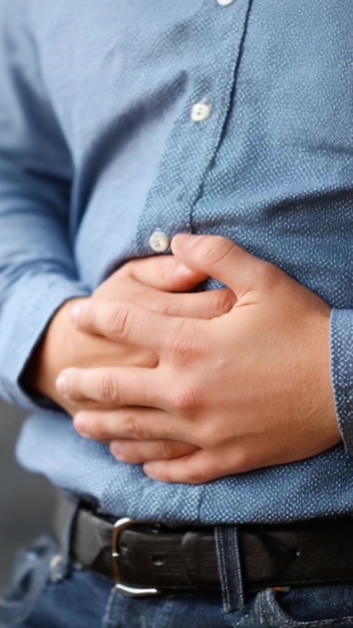 Una persona experimentando malestar estomacal mientras viste una camisa azul casual y jeans, indicando la necesidad de prestar atención a su bienestar físico y salud.