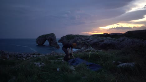 Un-Joven-Aventurero-Que-Acampa-Empaca-Una-Tienda-De-Campaña-Al-Amanecer-En-Un-Acantilado-Oceánico