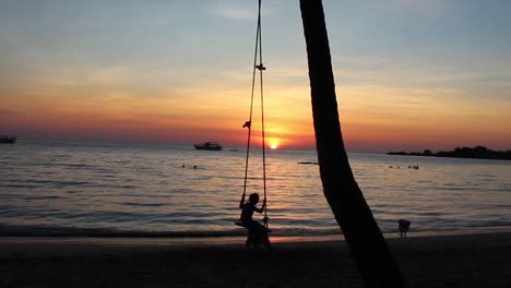 romantic holiday scenery of girl on swing at the beach during sunset