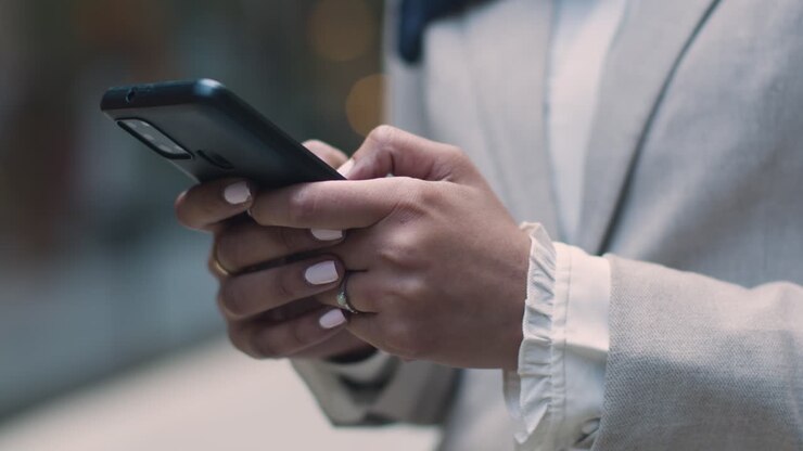 Close Up Of Muslim Businesswoman Checking Messages On Mobile Phone Standing Outside Office In City