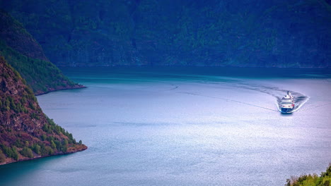 Time-lapse-shot-of-cruise-ship-on-fjord-between-mountains-during-sunny-day---aerial-wide-shot