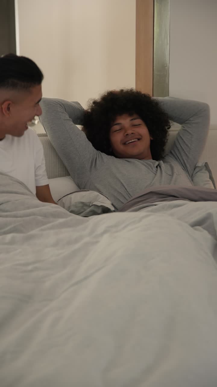 Vertikal video: To mænd reagerer på et vækkeur, der ringer, slukker det, putter i sengen og bruger fjernbetjeningen