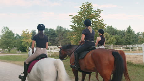 three female riders riding horses side by side near wood fencing, rear view