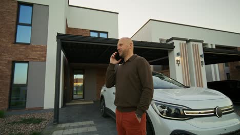 hombre hablando por teléfono fuera de su casa moderna