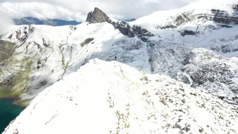 drone disparado volando rápido hacia adelante y pasando una sola persona de pie por sí solo en la parte superior del pico cerca del borde empinado y afilado de la cresta