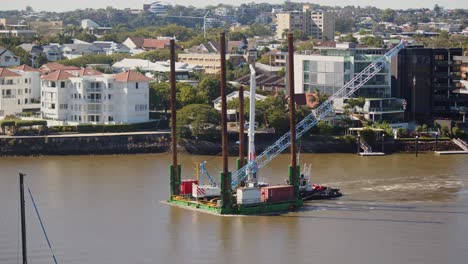 una barcaza de cubierta plana que transporta una pequeña grúa sobre orugas río arriba