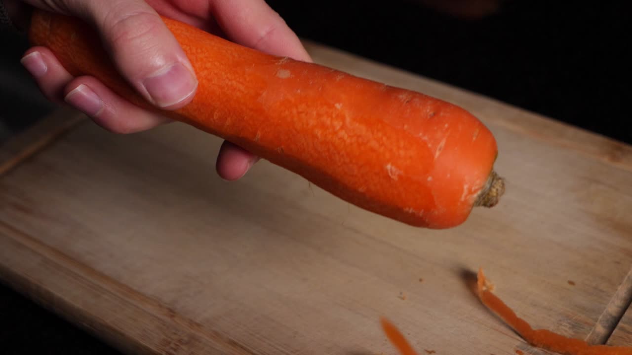 Mani di chef caucasico pelano una carota con un pelapatate verde, al rallentatore