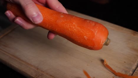 caucasian chef hands peels a carrot with a green peeler in slow motion