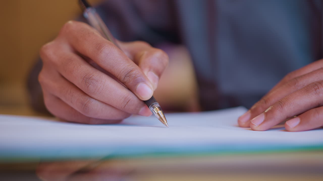 Close-up of male hands holding pen and writing or sketching on white paper during work or planning session, capturing moment of focus, creativity, and detail in calm indoor environment
