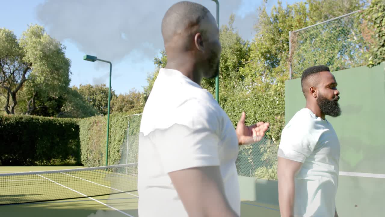 Two male tennis players with rackets stepping to net and high-fiving after rally, dust drifting