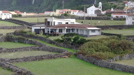 Toma-Inclinada-Hacia-Arriba-De-Una-Villa-En-Fajã-Grande-Con-Cascada-Al-Fondo,-Aérea