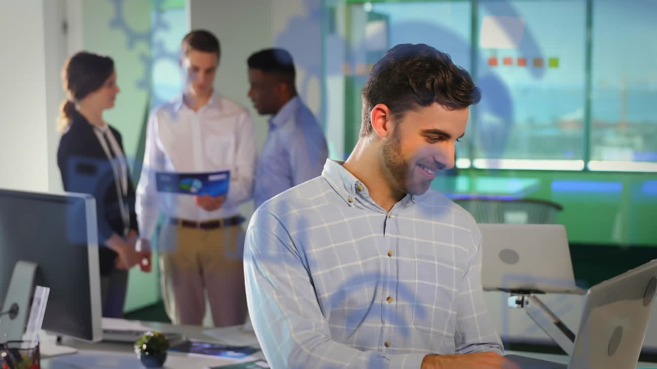 animación de múltiples iconos digitales sobre un hombre caucásico usando una computadora portátil y sonriendo en la oficina.