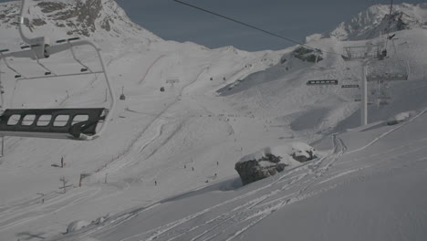 wide shot from above in a ski elevator looking at the slopes and some empty ski seats on a sunny day log