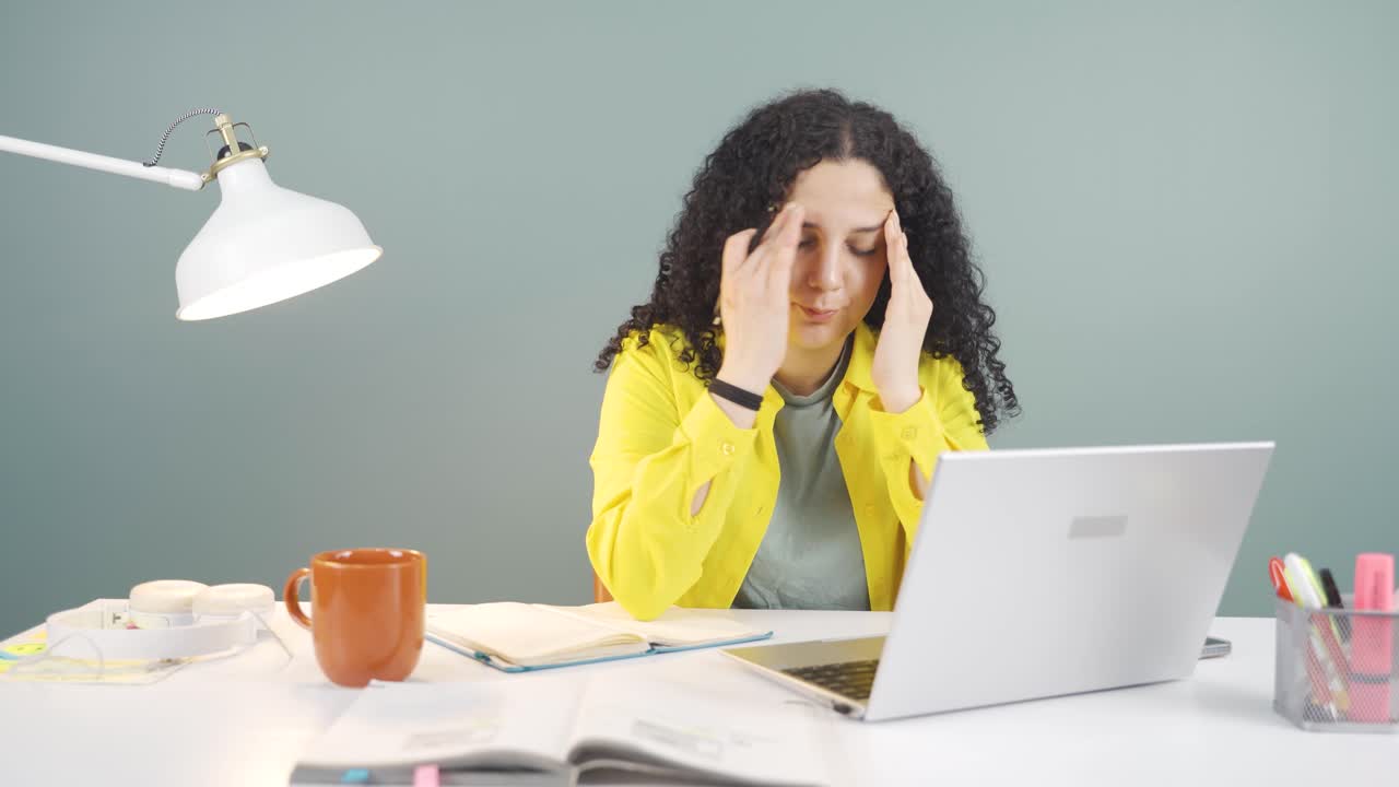 una mujer joven que trabaja en una computadora portátil tiene dolor de cabeza.