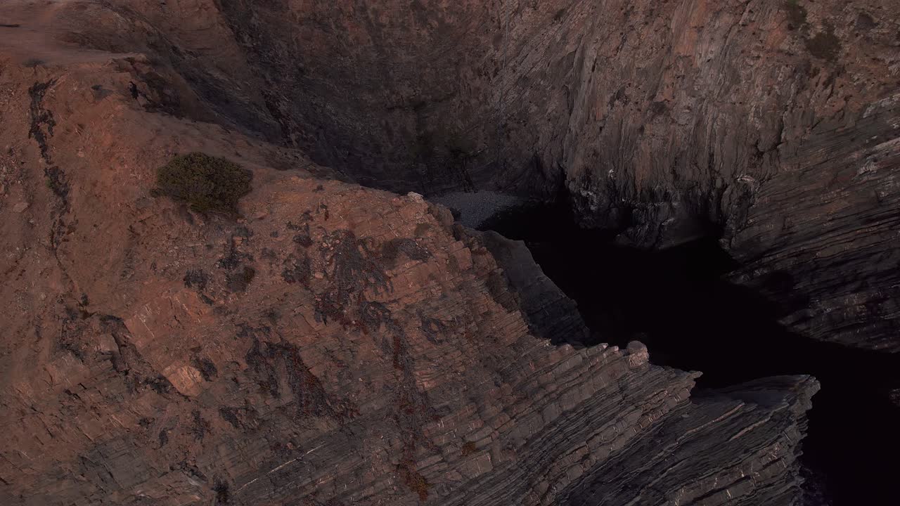 Scogliere sedimentarie stratificate a Cabo Sardão nel Parco Naturale della Costa Vicentina São Teotónio Odemira Portogallo con un uomo solitario in piedi sul bordo della scogliera sopra l'Oceano Atlantico, orbita aerea con drone e ripresa in discesa
