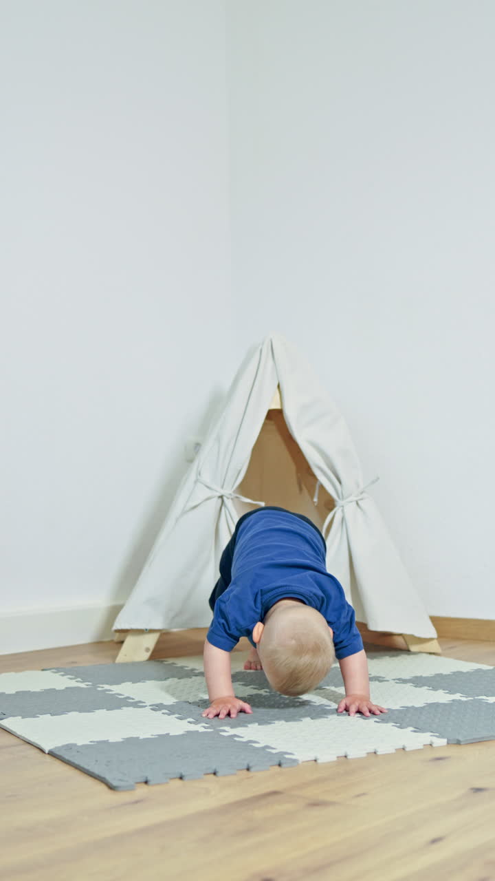 Cheerful toddler boy playing at home on a rug and sitting in a wigwam. A house for a child in an apartment. A wigwam for a child. A child in the living room is mischievous and laughing